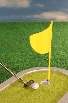 Golf game with putter, golf ball and a flag on the lawn before a blue sky