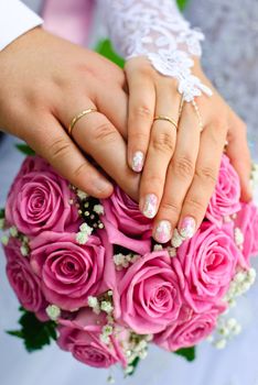 Hands of bride and groom with wedding rings over the bridal bouquet