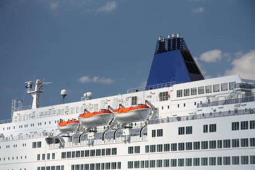 Detail of a middle sized cruise ship with blue chimney and saving vessels