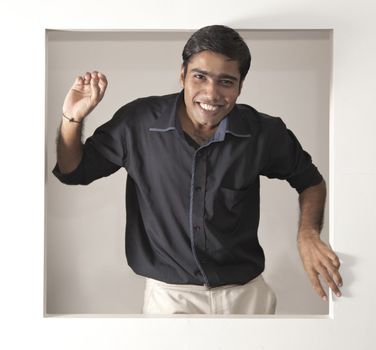 young Indian man looking happy in a black short beige pants looking out of a window