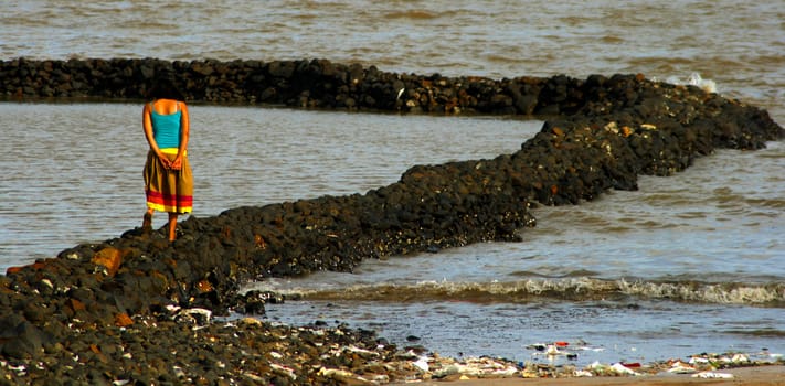 Solitary Indian lady walking on rocky beach, waves, seashore