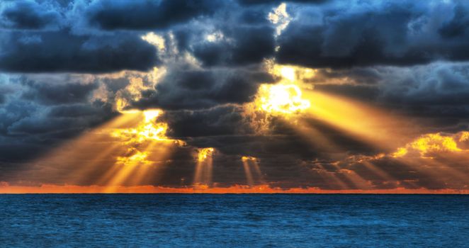 Dramatic sunset rays through a cloudy dark sky over the ocean.
