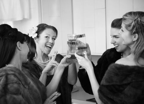 Group of four women with fur coats raising a toast in a kitchen