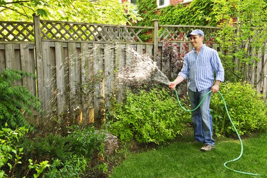 Man watering the garden with hose in backyard