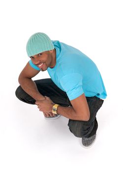 Smiling young man in a blue t-shirt squatting. Isolated on white background.