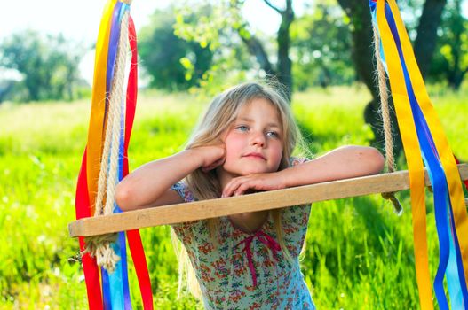 Young cute girl on swing with ribbons in the garden