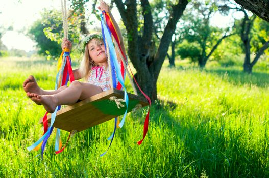 Young cute girl on swing with ribbons in the garden