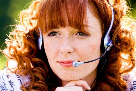 Close-up portrait of red-haired lovely young woman with headset outdoors