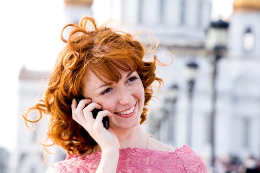 Smiling red-haired young woman talking on mobile phone outdoors
