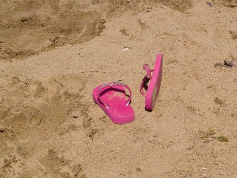 Kid's sandals sitting in the sand, kicked off by the child.