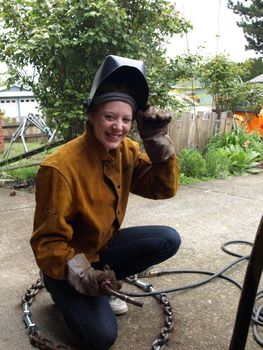 A female welder lifts her welding mask and smiles brightly.