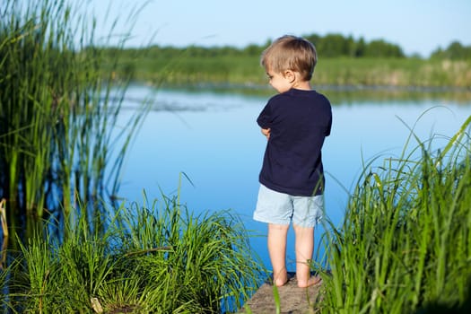 Cute 2 years old boy stands and looking at the river