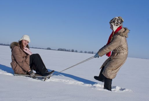 Two happy sisters sledding at winter time