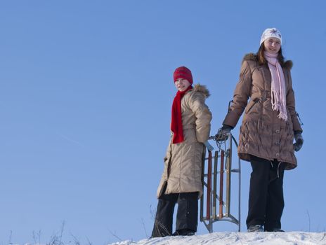 Two happy sisters sledding at winter time