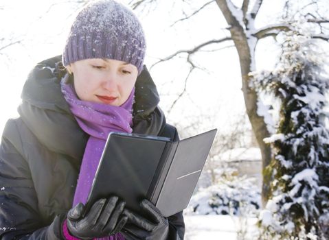 Young lady reading e-book outdoors at winter time
