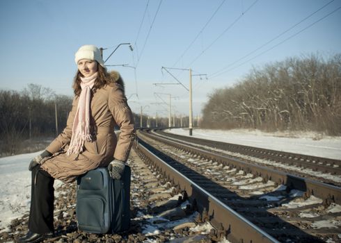 Teen girl with a suitcase near the railways at winter time