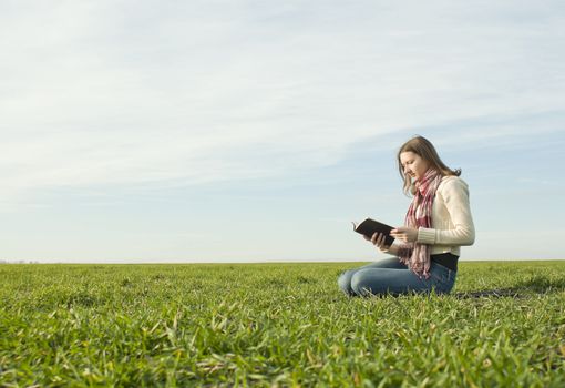 Teen girl reading a book sitting at grass