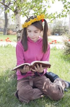 Teen girl reads book sitting on grass
