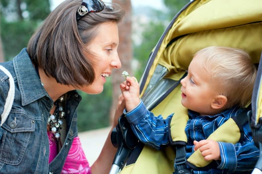 Cute 2 years old boy shows his mother a flower in the park