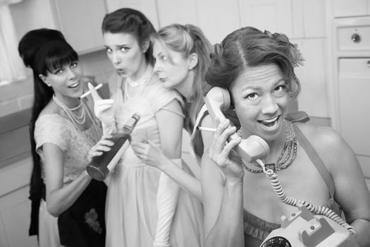 Excited woman on phone while friends drink and smoke in the kitchen