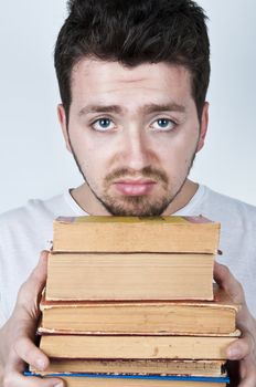 Young man holding a stack of old books looking bored and unhappy