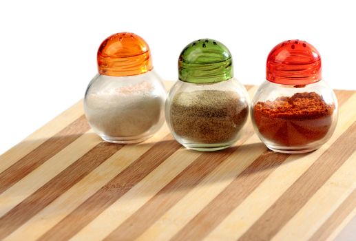 Salt, black pepper, paprica boxes  on wooden striped plate on white background