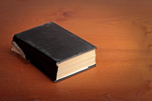 Old black covered book on the brown scratched table