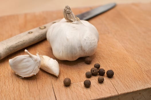 Garlic, kitchen knife and allspice on chopping board