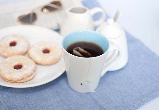 Mug of Tea, Cookies, Cream Pot, Sugar Basin and Newspapers with Glasses on Table