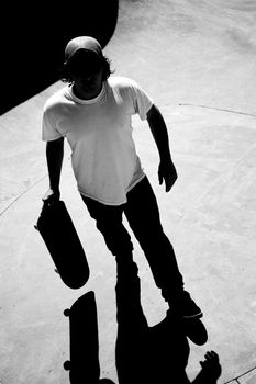 Silhouette of a skateboarder standing inside the pool at the skate park with strong contrast and dramatic shadows. Black and white.