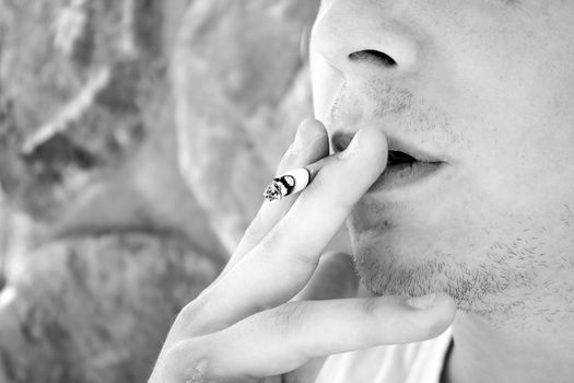 Close up of a young man smoking a cigarette taking a drag in black and white.  Shallow depth of field.
