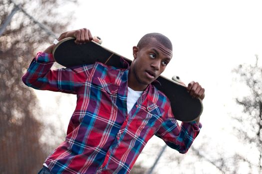 A young man hanging out holding his skateboard on the back of his shoulders over his head.