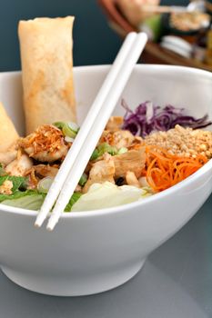 Freshly prepared Thai salad with spring rolls in a bowl with some chopsticks.