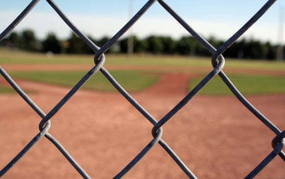 A view of a baseball diamond behind the fench with the chains links in focus.