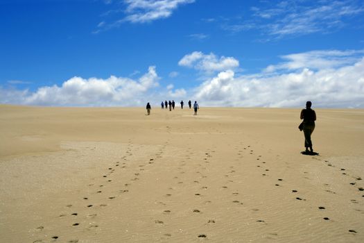 Group of people walking on sand dunes.
