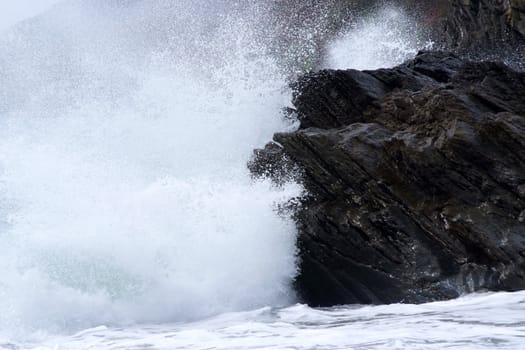 The sea crashing against dark tough rocks