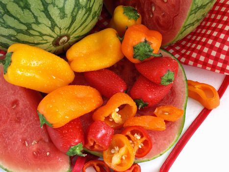 A vibrant summer crop of fresh juicy watermelon and colorful bell peppers, with water drops, studio isolated over a white background.