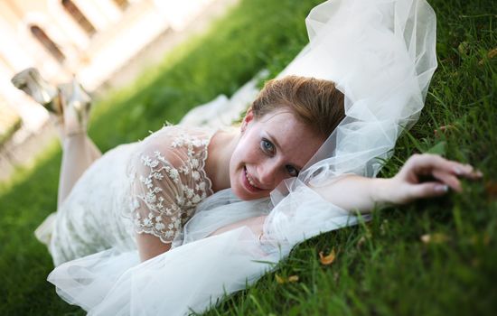 The beautiful bride with a wedding bouquet lays on a grass