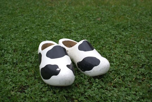 Wooden shoes with cow print standing in grass.