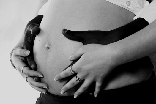 Portrait of a pair of black hands on a caucasian white pregnant belly