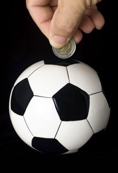 A coin is deposited into a piggybank that resembles a soccer ball.
