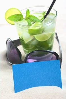 Blank blue card on sand with sunglasses and a mojito cocktail in the back (Selective Focus, Focus on the card)