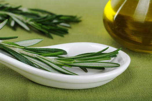 Rosemary on ceramic spoon with olive oil in glass bottle on green textile (Selective Focus) 