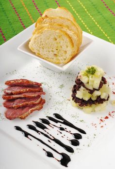 Appetizer: Duck meat, blood sausage, apples and baguette slices on white plate and green table mat (Selective Focus) 