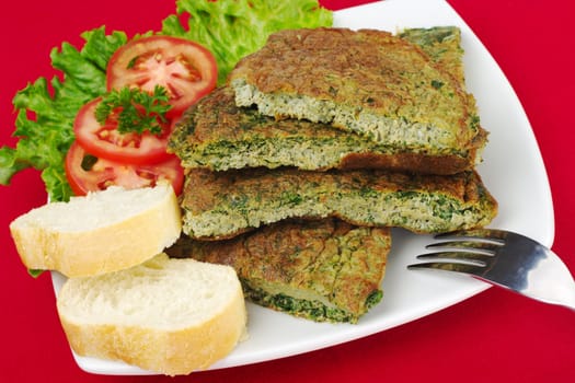 Omelette with herbs with fork, lettuce, tomato, parsley and baguette, on white plate and red tablecloth (Selective Focus)