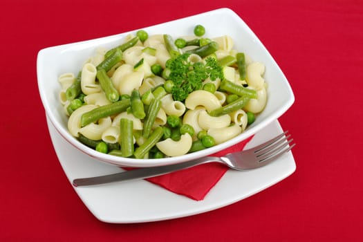 Pasta with peas, green beans, zucchini and spring onions and parsley on red tablecloth (Selective Focus) 