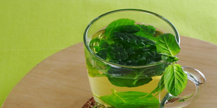 Fresh mint tea in glass cup with mint leaves on wooden board and green tablecloth (Selective Focus)