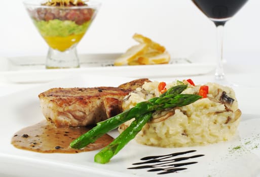 Green asparagus with rice, meat and gravy with red wine and appetizer in the background (Selective Focus)