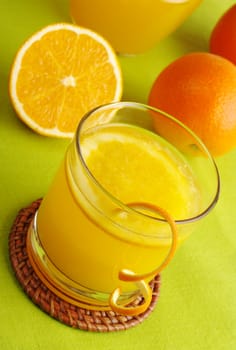 Fresh orange juice with orange slice in glass and oranges in background on green table mat (Selective Focus)