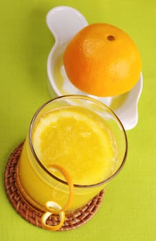 Fresh orange juice with orange slice in glass and squeezer in background on green table mat (Selective Focus)